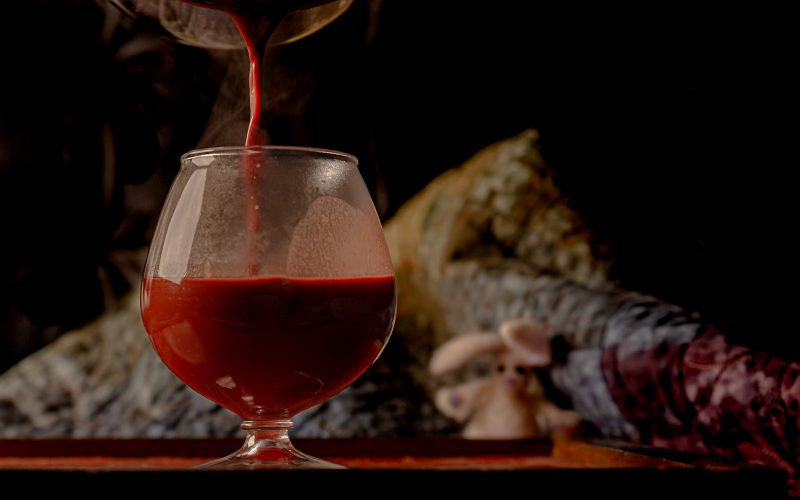 Glass being filled with steaming red liquid with a blurred figure holding a stuffed rabbit in the background.